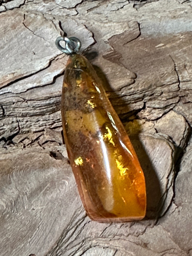 May include: A teardrop-shaped amber pendant with a silver bail. The amber is a warm honey colour with inclusions of plant matter.