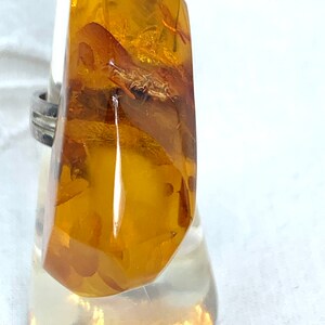 May include: A silver ring with a large, amber gemstone. The amber is a deep, golden color and has inclusions of plant matter.