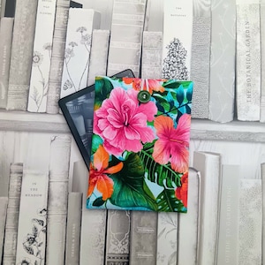 Peut inclure: Une housse pour liseuse de couleur bleu sarcelle et blanche à fleurs avec un bouton vert. La housse présente des fleurs d'hibiscus roses et orange et des feuilles vertes.