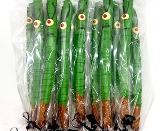May include: A dozen green pretzel rods dipped in chocolate and decorated with a single red eye and two white eyebrows. The pretzel rods are individually wrapped in clear plastic bags and tied with black ribbon.