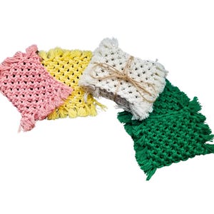 May include: Four crocheted coasters in pink, yellow, white, and green. Each coaster has a fringe border.