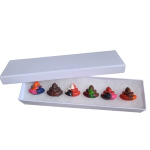 May include: A set of six colorful poop-shaped crayons in a white box. The crayons are arranged in a row and are all different colors, including red, orange, yellow, green, blue, and brown.