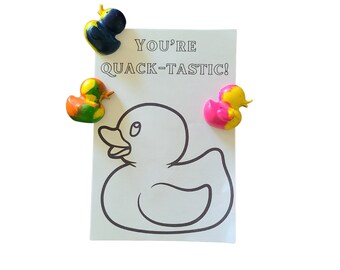 May include: A white card with the text "You're Quack-Tastic!" and a black and yellow rubber duck, a green and yellow rubber duck, and a pink and yellow rubber duck. The card has a black and white outline of a rubber duck.