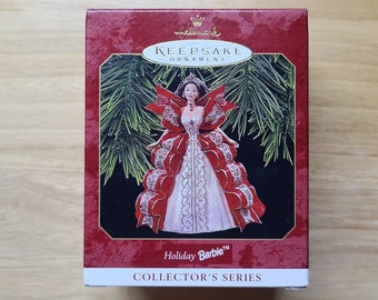 May include: A red and white Hallmark Keepsake Ornament featuring a Barbie doll dressed in a white gown with a red bow and a red and white trim. The ornament is in its original box, which is red with gold lettering. The text on the box reads "Holiday Barbie Collector's Series".