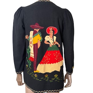 May include: A black long-sleeved jacket featuring an embroidered applique on the back depicting a person in a sombrero and a person in a red and green dress. The design includes a cactus, small flowers, and decorative trim along the edges.