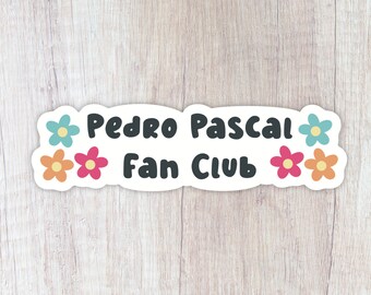 May include: A white sticker with the text "Pedro Pascal Fan Club" in black, surrounded by four colorful flowers. The flowers are blue, pink, and orange.