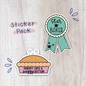 May include: A sticker pack with two stickers. One sticker is a blue and white ribbon with a star and the text "Star Baker". The other sticker is a pink pie with the text "Nobody likes a soggy bottom".