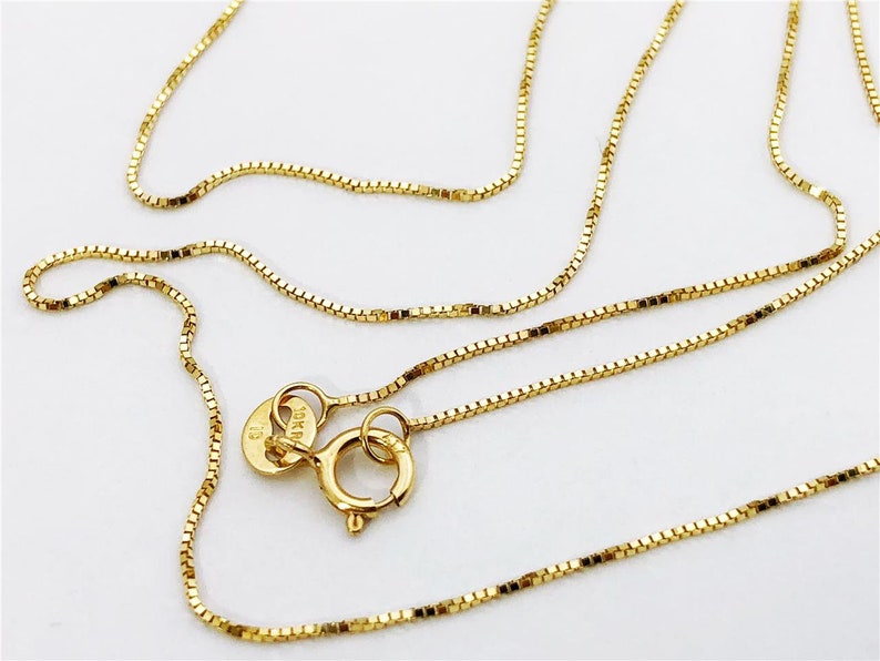 May include: A gold chain necklace with a box chain style. The chain has a lobster clasp and a tag that reads "10K" and "13".