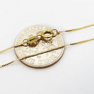 May include: A gold chain necklace with a lobster clasp. The chain is laid on top of a US dime coin for size comparison.