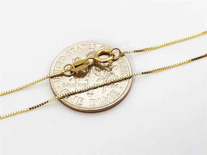 May include: A gold chain necklace with a lobster clasp. The chain is laid on top of a US dime coin for size comparison.