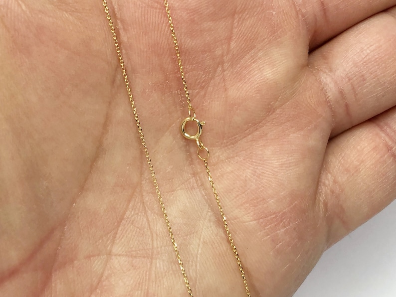 K&ouml;nnte beinhalten: Eine goldene Kettenkette mit einem Karabinerverschluss.