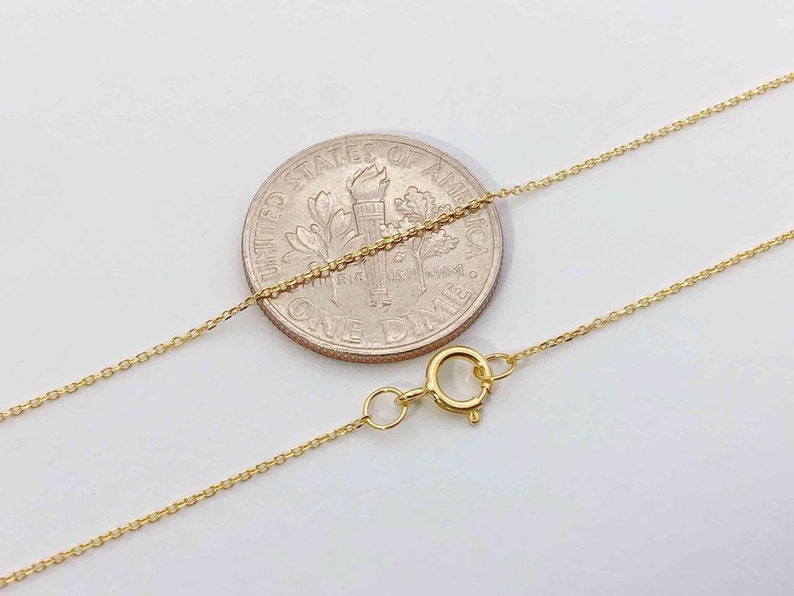 K&ouml;nnte beinhalten: Eine goldene Kettenkette mit einem Karabinerverschluss. Die Kette wird neben einem US-Dime zur Gr&ouml;&szlig;enbestimmung gezeigt.