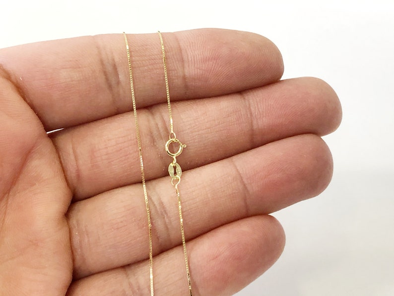 May include: A gold chain necklace with a box clasp. The chain is thin and delicate.