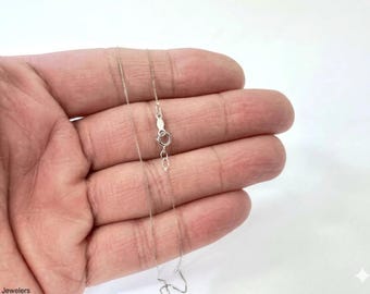 May include: A thin, silver-colored metal chain necklace featuring a small, circular spring ring clasp. The delicate chain links are uniform in size and shape, creating a smooth, continuous appearance. The clasp is positioned near the center.