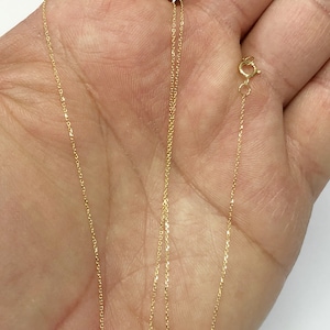 K&ouml;nnte beinhalten: Eine goldene Kettenkette mit einem Karabinerverschluss. Die Kette ist zart und hat eine feine, glatte Textur.