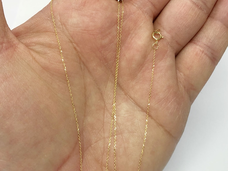 K&ouml;nnte beinhalten: Eine goldene Kettenkette mit einem Karabinerverschluss. Die Kette ist zart und hat eine feine, glatte Textur.