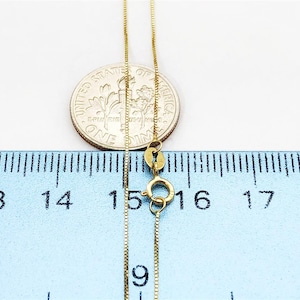 May include: A gold chain necklace with a lobster clasp, measured against a ruler. The chain is 16 inches long.