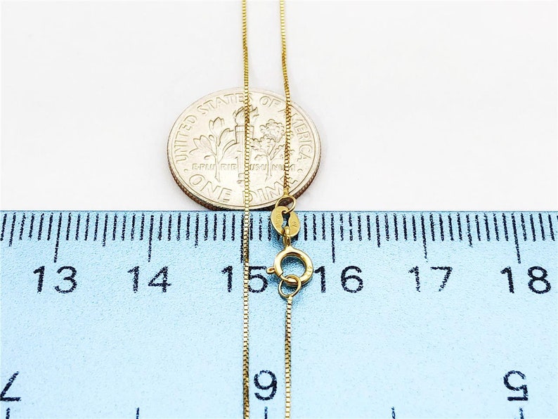 May include: A gold chain necklace with a lobster clasp, measured against a ruler. The chain is 16 inches long.