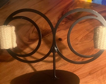 May include: A black metal stand with two circular rings and a round base. Two white fabric rolls are placed on the rings.