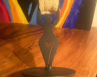 May include: A black metal figurine of a woman holding a roll of twine. The figurine is standing on a round base with a metal bar extending from the base.