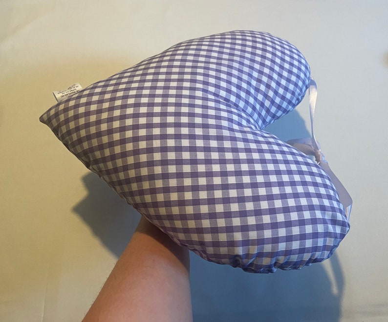 Op de afbeelding: Een hartvormig kussen met een paars-wit geruit patroon. Het kussen heeft een wit lint eromheen gebonden.