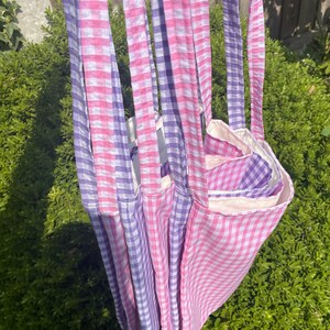 Op de afbeelding: Vier tote bags van roze en paarse gingham stof. De tassen zijn op elkaar gestapeld en hebben een witte voering van stof.