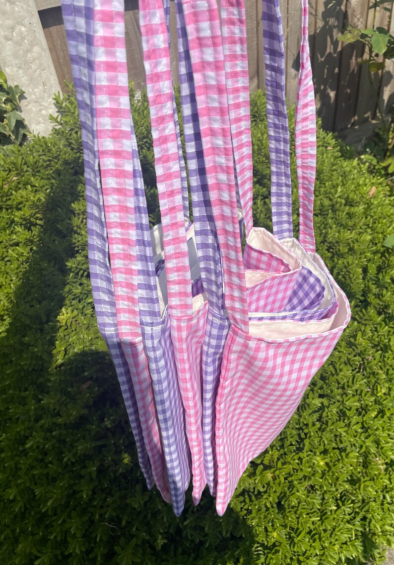Op de afbeelding: Vier tote bags van roze en paarse gingham stof. De tassen zijn op elkaar gestapeld en hebben een witte voering van stof.