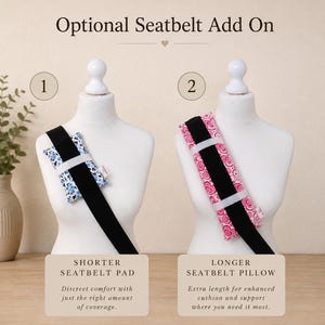 May include: Two white mannequins display seatbelt accessories. The left shows a shorter blue and white floral seatbelt pad. The right shows a longer pink heart-patterned seatbelt pillow. Both are attached to black straps with white elastic bands.