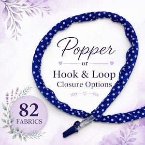 May include: A blue fabric tube with a white polka dot pattern, featuring a clear plastic connector at one end. The text reads: Popper or Hook & Loop Closure Options, and 82 FABRICS. The design includes small purple heart and leaf illustrations.