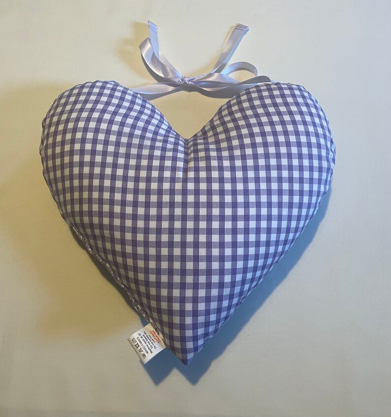 Op de afbeelding: Een hartvormig kussen van paars en wit gingham met een wit satijnen lint dat bovenaan is gebonden.