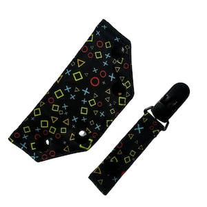 May include: Black fabric baby bib and pacifier clip set. The bib has a triangular shape with snaps and a pattern of colorful geometric shapes. The pacifier clip is a matching black fabric with a clip and snap closure.