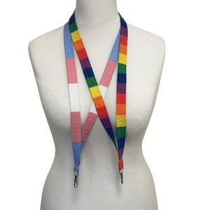 Könnte beinhalten: Ein farbenfrohes Schlüsselband mit Regenbogenmuster und Transgender-Pride-Flagge. Das Schlüsselband wird auf einer weißen Schaufensterpuppe präsentiert und hat silberne Metallverschlüsse an den Enden.