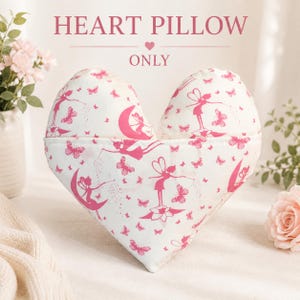 May include: A heart-shaped pillow with a white background and a repeating pattern of pink fairies and butterflies. The text HEART PILLOW ONLY is printed in pink above the pillow. The design features fairies sitting on moons and flowers.