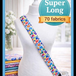 May include: A long fabric strap featuring a colorful heart pattern draped over a white mannequin torso. A teal circular graphic with the text Super Long 70 fabrics is visible. The strap has a black end piece and is displayed with a measuring tape.