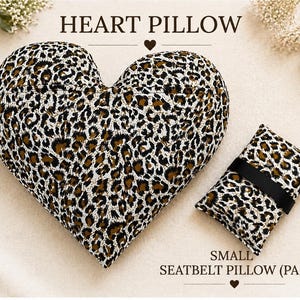May include: A heart-shaped pillow and a small rectangular seatbelt pillow, both featuring a brown, black, and white leopard print pattern. The text HEART PILLOW is centered above the heart, and SMALL SEATBELT PILLOW (PAD) is below the rectangular pad.