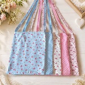 Könnte beinhalten: Eine Auswahl an Stoff-Tragetaschen in Pastelltönen. Die Taschen zeigen Blumen- und Polka-Dot-Muster in Blau, Rosa und Weiß. Jede Tasche hat Träger aus passendem Stoff.