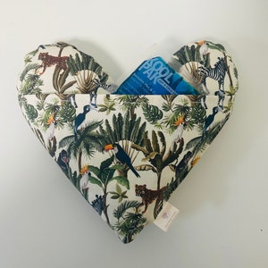 May include: A heart-shaped, white fabric hot or cold pack with a jungle print. The pack has a blue gel pack inside and features a variety of animals, including parrots, toucans, monkeys, and zebras. The text "Kool Pak" is printed on the gel pack.