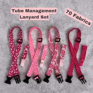 May include: A set of pink and red tube management lanyards with various patterns, including polka dots, floral, and heart designs. Each lanyard has a black buckle and a matching pink clip. The text "Tube Management Lanyard Set" and "70 Fabrics" are visible.