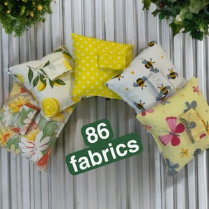 May include: A selection of small, square fabric cushions in various patterns. Designs include lemons, bees, butterflies, and polka dots. The text "86 fabrics" is displayed on a green rectangular sign.