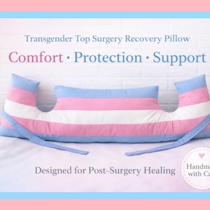 May include: A recovery pillow designed for post-surgery healing. The pillow features a blue, pink, and white striped design, with the words "Comfort, Protection, Support" printed on the front. The pillow is handmade with care.