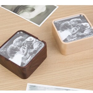May include: Two wooden photo boxes with a square shape. One box is light brown and the other is dark brown. Both boxes have a clear glass insert that displays a black and white photo of two children.