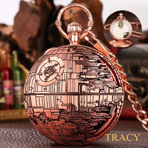 May include: A rose gold pocket watch with a detailed design of the Death Star from Star Wars. The watch has a chain attached to it and the face of the watch is visible in the background.
