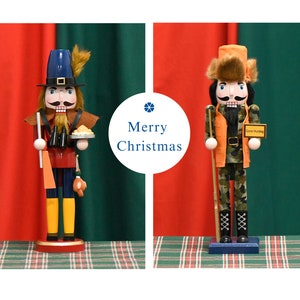 May include: Two wooden nutcracker figurines, one dressed as a pilgrim with a pie and the other dressed as a hunter with a gun. The background is red and green plaid.