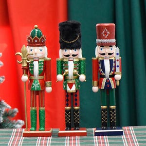 May include: Three wooden nutcracker figurines, each with a different design. The first is a traditional red and green nutcracker with a gold crown and a spear. The second is a green and red nutcracker with a black hat and drumsticks. The third is a red and blue nutcracker with a red hat and a sword.