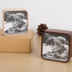 May include: Two wooden music boxes with a black and white photo of a young couple kissing. The music boxes are square and have a clear glass front.