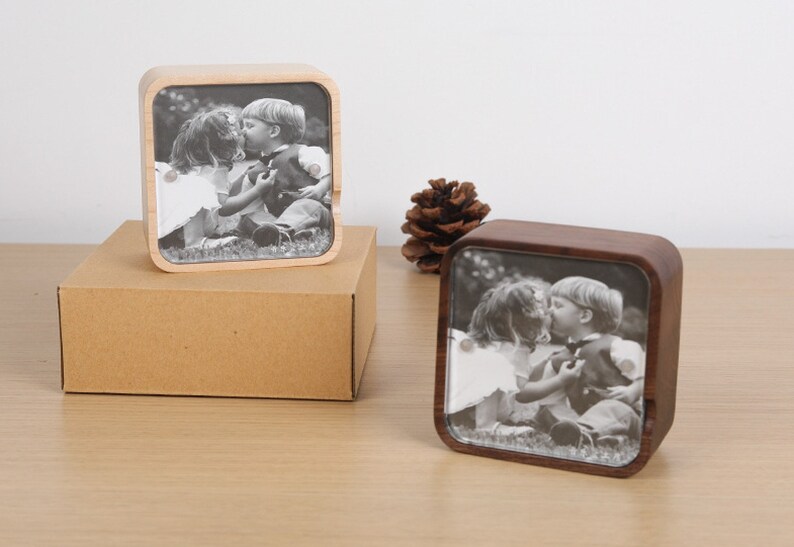 May include: Two wooden music boxes with a black and white photo of a young couple kissing. The music boxes are square and have a clear glass front.