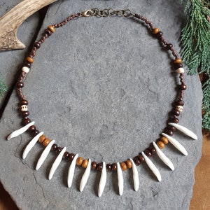 May include: A brown leather cord necklace with brown and white wooden beads and white ceramic teeth pendants.