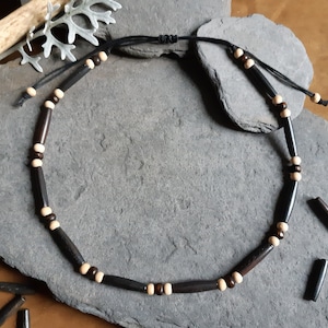 Puede incluir: Un collar de cuentas negras y blancas con un cordón negro. El collar está hecho de cuentas de madera y tiene un diseño simple.