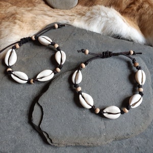 Puede incluir: Dos pulseras de cuero marrón con abalorios de concha blanca y cuentas de madera.