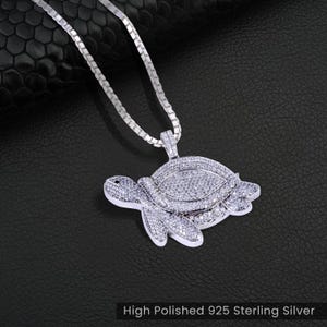 Könnte beinhalten: Eine silberne Kettenkette mit einem Schildkrötenanhänger. Die Schildkröte ist mit klaren Zirkonia-Steinen besetzt. Hochglanzpolierter 925er Sterlingsilber.